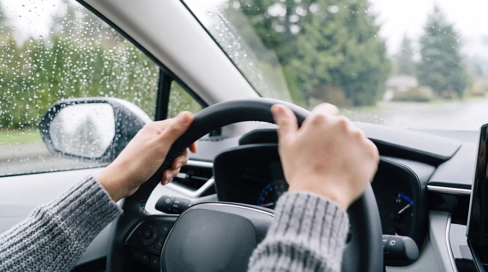 Both hands on the steering wheel as rain streaks the windshield